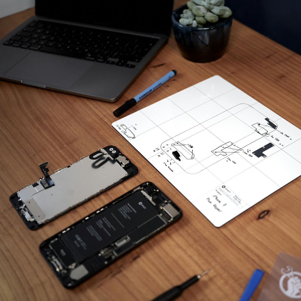 iPhone 7 Plus taken apart on work bench with iFixit magnetic mat keeping track of screws